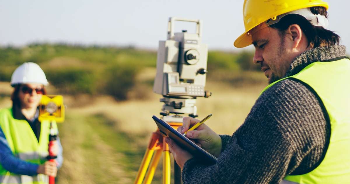 a surveyor near a theodolite, writing on a clipboard